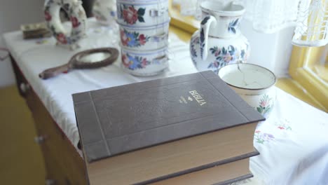 Old-Hungarian-Bible-on-table-with-vintage-bowl,-pitcher,-mirror-in-old-house