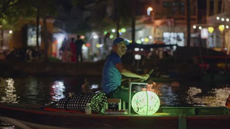 Hombre-Vietnamita-Remando-Bote-Iluminado-Por-Una-Linterna-En-La-Noche-En-Hoi-An,-Vietnam