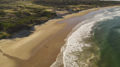 Aerial-orbiting-shot-of-man-at-sandy-beach-stretching-in-front-of-Atlantic-ocean---Beautiful-landscape-with-dunes-in-Uruguay-at-sunset