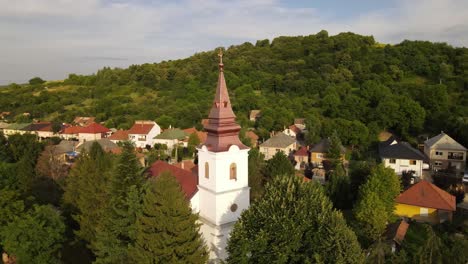 Aerial-parallax-around-steeple-of-small-church-in-village-near-Varbo,-Hungary