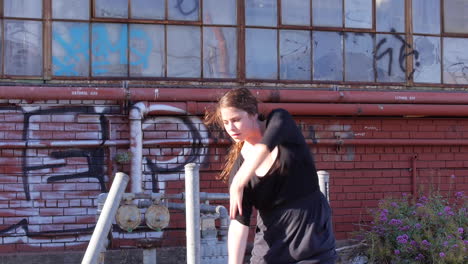 White-Woman-in-Ponytail-Dancing-In-Front-of-Industrial-Warehouse