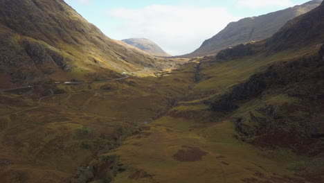 Scottish-highway-winds-along-rugged-highland-valley,-aerial-view