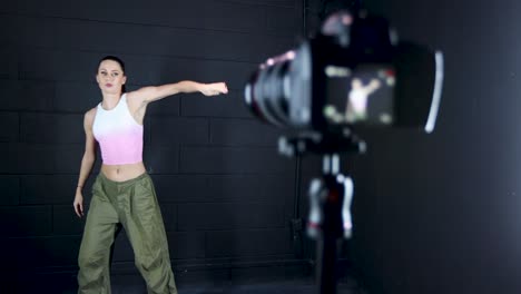 camera-on-a-tripod-filming-a-female-caucasian-dancer-performing-in-a-studio-with-a-black-wall