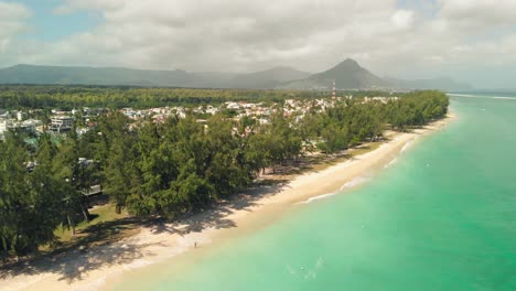 Town-surrounded-by-trees-next-to-the-beach-with-mountains-in-the-background