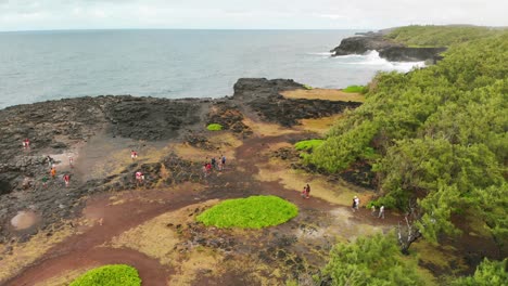 Top-view-of-people-walking-to-the-Pont-Naturel-on-a-cliff-covered-with-volcanic-rocks-in-Mauritius