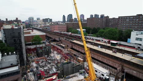 Construction-crane-at-a-train-station-in-Harlem,-NYC,-USA---Ascending-aerial-view