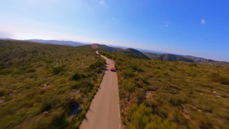 Aerial-drone-view-following-a-red-sportscar-driving-through-the-scenic-countryside-of-Catalonia,-Spain