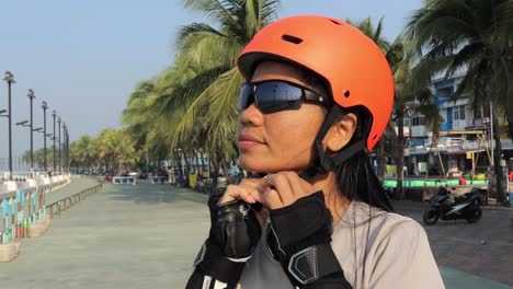 Female-Inline-Skater-Puts-On-Protective-Helmet,-Preparing-To-Skate-At-The-Park-In-Thailand