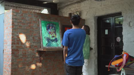 a-man-in-a-blue-shirt-and-a-man-in-a-green-shirt-looking-at-an-abstract-portrait-painting,-discussing-feedback-of-art