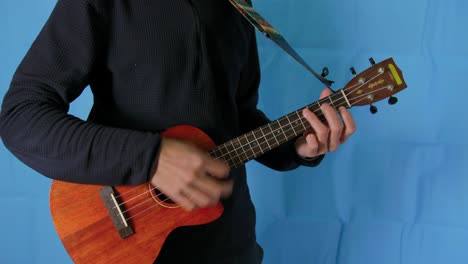 Static-close-up-of-a-musician-man-playing-ukelele-with-blue-studio-background