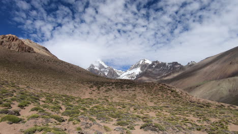 View-of-the-summit-of-Aconcagua-from-the-approach-to-basecamp,-with-blue-sky-and-clouds-moving-over-the-mountains-creating-shadows-in-the-valley
