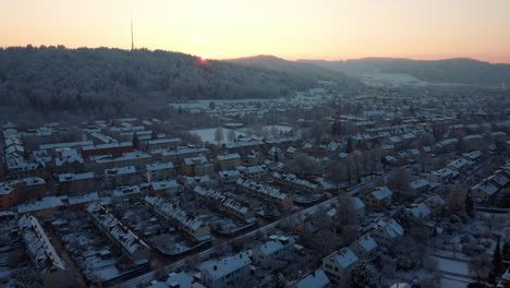 Aerial-view-of-snow-covered-houses-of-Winterthur,-flying-towards-the-setting-sun-on-a-beautiful-winter-day