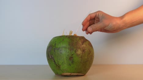 Person-inserting-a-straw-into-a-delicious-green-coconut-in-slow-motion