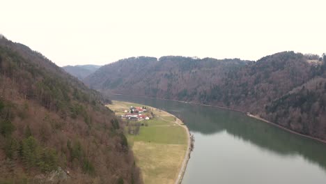 Luftaufnahme-An-Einem-Düsteren-Tag-Entlang-Der-Donau-In-Richtung-Eines-Kleinen-Dorfes-In-Oberösterreich