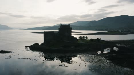 Drone-shot-approaching-the-silhouette-of-a-castle-on-an-island-in-Scotland's-countryside