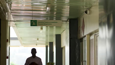 Zeitlupenaufnahme-Eines-Mannes,-Der-Unter-Einem-Medizinischen-Schild-Im-Flur-Des-Krankenhauses-In-Ruanda-Steht