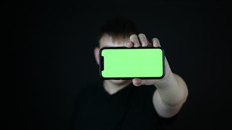 Junger-Mann-Mit-Klebeband-über-Dem-Mund-Zeigt-Smartphone-Mit-Grünem-Bildschirm