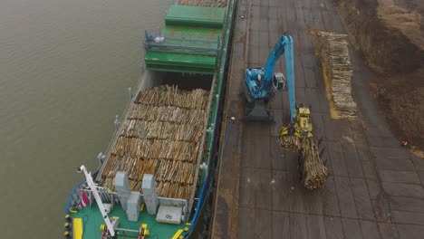 Aerial-establishing-view-of-wood-terminal-crane-loading-timber-into-the-cargo-ship,-Port-of-Liepaja-,-lumber-log-export,-overcast-day-with-fog-and-mist,-birdseye-drone-shot