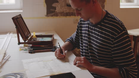 Young-architecture-student-drawing-sketch-with-pencil-at-his-desk