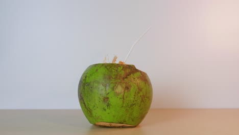 Person-leaving-a-green-coconut-with-a-straw-on-the-table-ready-to-drink