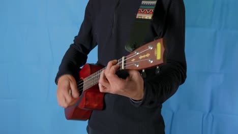 Close-up-of-an-unrecognizable-person-playing-the-ukele-in-a-room-with-a-blue-background