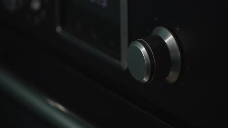 Person-turning-up-temperature-knob-of-black-oven-in-home-kitchen,-close-up