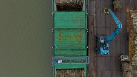 Aerial-birdseye-view-of-wood-terminal-crane-loading-timber-into-the-cargo-ship,-Port-of-Liepaja-,-lumber-log-export,-overcast-day-with-fog-and-mist,-wide-drone-shot-moving-backward