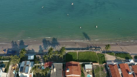 Truck-left-aerial-drone-shot-of-the-tropical-Bessa-beach-in-the-capital-city-of-Joao-Pessoa,-Paraiba,-Brazil-with-people-enjoying-the-ocean-surrounded-by-palm-trees,-beach-houses,-and-fishing-boats