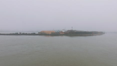 Aerial-establishing-view-of-wood-terminal-crane-loading-timber-into-the-cargo-ship,-Port-of-Liepaja-,-lumber-log-export,-overcast-day-with-fog-and-mist,-wide-drone-drone-shot-moving-forward