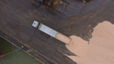 Aerial-birdseye-view-of-wood-terminal,-truck-unloading-wood-chip-cargo-into-the-large-pile,-Port-of-Liepaja-,-lumber-log-export,-overcast-day-with-fog-and-mist,-orbiting-drone-shot