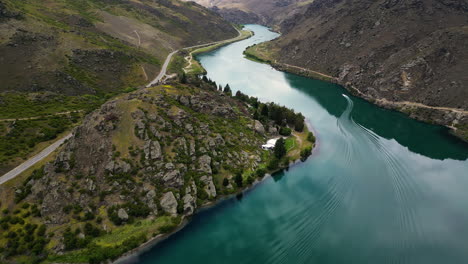 Motorboat-enters-Cromwell-gorge-on-Clutha-River,-New-Zealand,-aerial-view