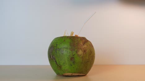 Close-up-of-a-person-leaving-on-the-table-in-slow-motion-a-cut-green-coconut-with-a-straw-ready-to-drink