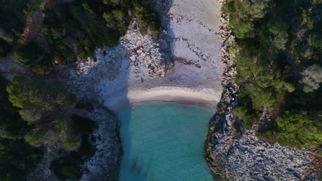 Aerial-View-of-clear-blue-water-crashing-on-shore-of-Es-Talaier-Virgin-Beach-in-Menorca-Spain-Wide-Shot