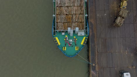Aerial-birdseye-view-of-wood-terminal-crane-loading-timber-into-the-cargo-ship,-Port-of-Liepaja-,-lumber-log-export,-overcast-day-with-fog-and-mist,-wide-drone-shot-moving-backward,-tilt-up