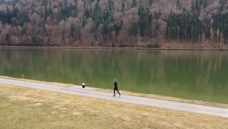panning-the-drone-that-filmed-this-footage-flies-next-to-a-path-where-a-jogger-in-a-black-suit-is-running