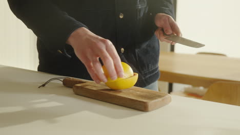 Male-cutting-grapefruit-in-halfs-on-a-wooden-cutting-board-with-sharp-knife-in-the-kitchen-at-home-4k
