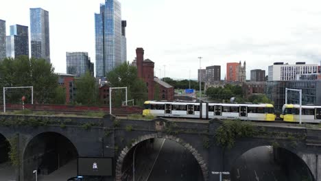 Aerial-drone-flight-flying-alongside-a-tram-on-a-bridge-in-Manchester-City-Centre-with-a-view-of-Elizabeth-towers-skyscrapers-in-the-background