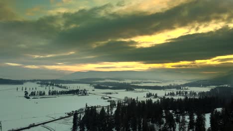 Dramatic-Yellow-Sky-over-Farmland-in-Enderby,-British-Columbia,-snowcovered-grassland-surrounded-by-evergreen-Forest