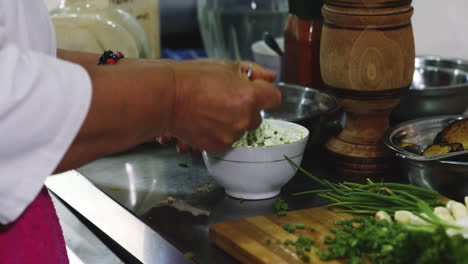 Old-chef-woman-stirring-and-tasting-herb-and-garlic-dip-in-kitchen