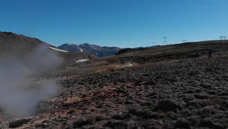 AERIAL---People-hiking-next-to-geysers,-Caviahue,-Argentina-Patagonia,-slowmo-circling