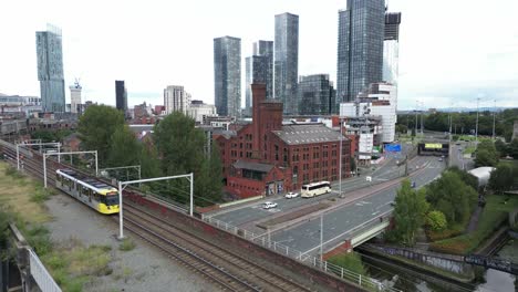 Aerial-drone-flight-over-a-moving-tram-and-Castlefield-Quays-Chimney-rooftops-to-slowly-reveal-Manchester-City-Centre-skyscrapers
