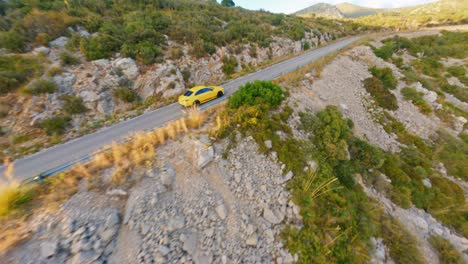 FPV-drone-tracking-a-yellow-race-car-speeding-along-a-mountain-highway-in-the-scenic-Spanish-countryside