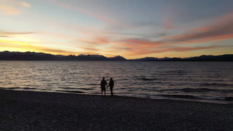 AERIAL---Two-people-at-sunset-next-to-lake,-Rio-Negro,-Patagonia,-Argentina,-circle-pan