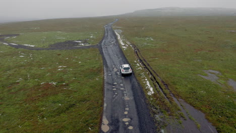 Aerial:-Following-a-white-car-on-muddy-dirt-road-while-snowing