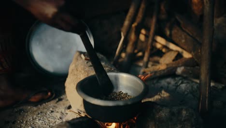 African-stirring-coffee-beans-in-metal-bowl-over-open-fire---roasting-coffee