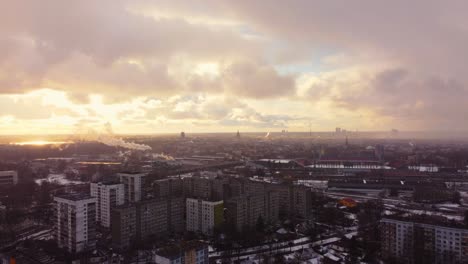 Golden-sunset-and-light-snowfall-over-Riga-city-suburbs,-aerial-view
