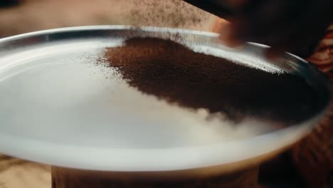 Traditional-Ugandan-sifter-used-to-sieve-dark-brown-ground-coffee-onto-big-plate