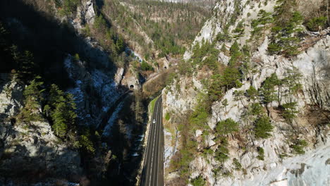 Cars-driving-over-the-road-in-the-Jura-Gorges-at-Moutier-in-Switzerland-next-to-a-rail-track-with-tunnels