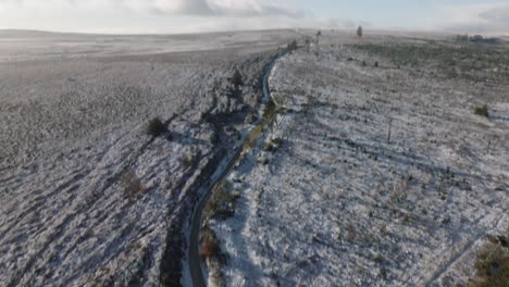Camera-panning-up-from-two-men-walking-along-a-frozen-path-to-show-a-wide,-open,-snowy-moorland-in-winter-sun