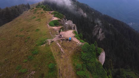 Aerial-circle-drone-shot-over-a-mountain-peak-with-3-hikers-admiring-and-epic-wide-landscape-of-a-valley